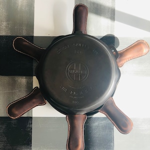 May include: A cast iron double skillet with leather handles. The skillet is labeled "Double Skillet 10" and "Griswold" with the text "Erie PA. U.S.A. Hand Cast in USA 1103".