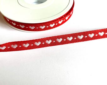 May include: Red ribbon featuring a repeating pattern of white hearts. The ribbon is spooled on a white plastic reel. Suitable for crafts, gift wrapping, or decorative use.