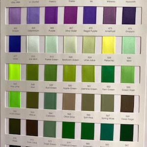 May include: A colour chart showing a selection of satin ribbon swatches. The chart presents a spectrum of colours, including purples, greens, and yellows, with each colour labelled with a number and name. The ribbons are arranged in neat rows.