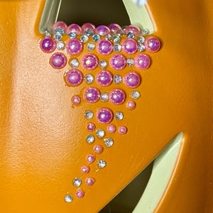Puede incluir: Primer plano de una calabaza con un dise&ntilde;o decorativo de diamantes de imitaci&oacute;n rosas y transparentes. Los diamantes de imitaci&oacute;n est&aacute;n dispuestos en forma de l&aacute;grima.