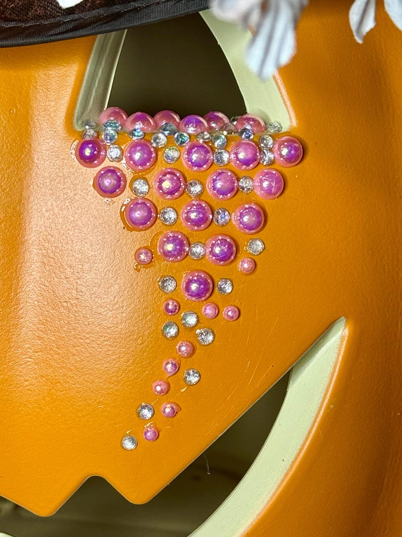 Puede incluir: Primer plano de una calabaza con un dise&ntilde;o decorativo de diamantes de imitaci&oacute;n rosas y transparentes. Los diamantes de imitaci&oacute;n est&aacute;n dispuestos en forma de l&aacute;grima.