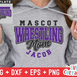 May include: Purple and black wrestling mom design with the text "MASCOT WRESTLING Mom JACOB" on a gray hoodie.