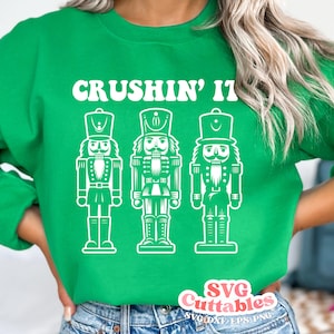 May include: Green sweatshirt with the text "CRUSHIN' IT" and three white nutcracker silhouettes.