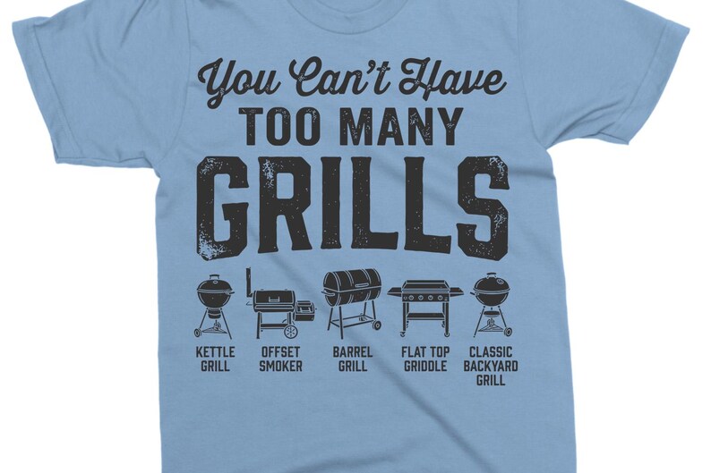 May include: Light blue t-shirt with the text "You Can't Have TOO MANY GRILLS" in a distressed font. Below the text are illustrations of different grill types: kettle, offset smoker, barrel, flat top griddle, and classic backyard grill.