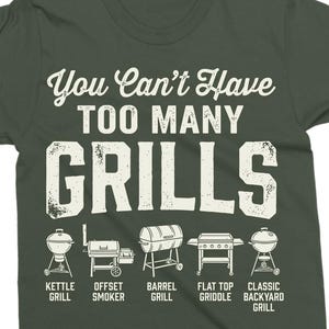 May include: Dark green t-shirt with the text "You Can't Have TOO MANY GRILLS" in white. Below the text are illustrations of different grill types: kettle, offset smoker, barrel, flat top griddle, and classic backyard grill.