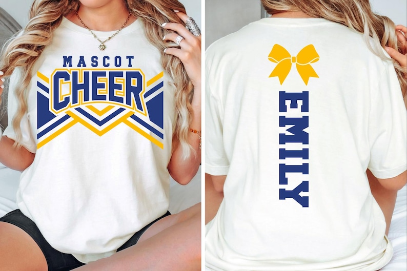 May include: A white t-shirt featuring a front graphic with the text MASCOT CHEER in blue and yellow, and a back graphic with a yellow bow icon above the vertical blue text EMILY. The shirt has short sleeves and a crew neckline, shown from both sides.