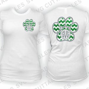 May include: Two white t-shirts with a green and silver paw print design. The paw print has a chevron pattern and a monogram in the center. The monogram is the letters "SVG".
