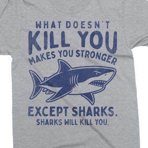 May include: A gray t-shirt with the text "WHAT DOESN'T KILL YOU MAKES YOU STRONGER EXCEPT SHARKS. SHARKS WILL KILL YOU." in blue. A blue shark graphic is centered below the text.