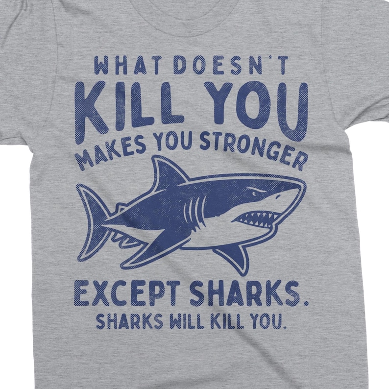 May include: A gray t-shirt with the text "WHAT DOESN'T KILL YOU MAKES YOU STRONGER EXCEPT SHARKS. SHARKS WILL KILL YOU." in blue. A blue shark graphic is centered below the text.