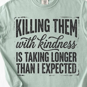 K&ouml;nnte beinhalten: Hellgr&uuml;nes T-Shirt mit dem schwarzen Aufdruck "KILLING THEM with kindness IS TAKING LONGER THAN I EXPECTED" in verblichener Schrift. Das T-Shirt hat hochgekrempelte &Auml;rmel und einen Rundhalsausschnitt.