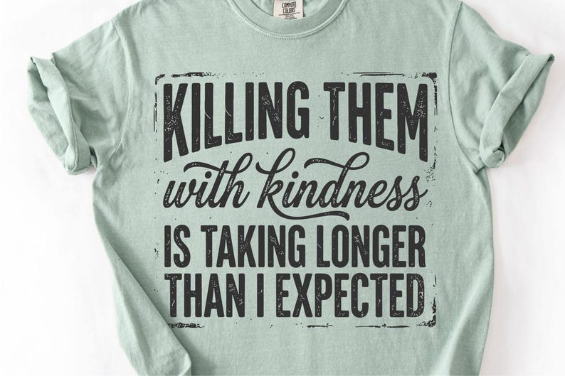 K&ouml;nnte beinhalten: Hellgr&uuml;nes T-Shirt mit dem schwarzen Aufdruck "KILLING THEM with kindness IS TAKING LONGER THAN I EXPECTED" in verblichener Schrift. Das T-Shirt hat hochgekrempelte &Auml;rmel und einen Rundhalsausschnitt.