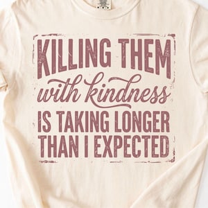 K&ouml;nnte beinhalten: Cremefarbenes T-Shirt mit dem Spruch "Killing them with kindness is taking longer than I expected" in verblichener, kastanienbrauner Schrift. Das Shirt hat kurze &Auml;rmel und einen Rundhalsausschnitt.