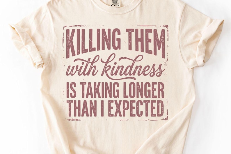 K&ouml;nnte beinhalten: Cremefarbenes T-Shirt mit dem Spruch "Killing them with kindness is taking longer than I expected" in verblichener, kastanienbrauner Schrift. Das Shirt hat kurze &Auml;rmel und einen Rundhalsausschnitt.
