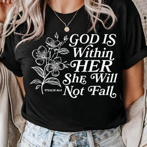May include: Black t-shirt with white text that reads "God is within her, she will not fall" and a floral design. The text also includes "Psalm 46:5".