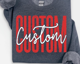 May include: A dark gray sweatshirt with the word "CUSTOM" in large red block letters and a white cursive "Custom" overlay. The sweatshirt has a crew neck and long sleeves with gray cuffs.