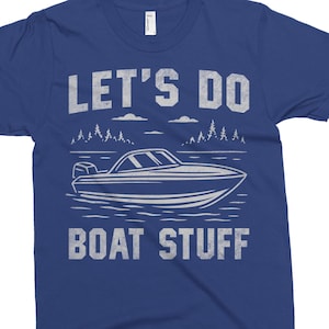 May include: A royal blue t-shirt with a white graphic design of a boat on a lake with trees and clouds. The text "Let's Do Boat Stuff" is printed in white below the boat.