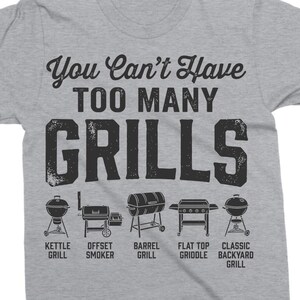 May include: A heather gray t-shirt with the text "You Can't Have Too Many Grills" in black. Below the text are illustrations of different grill types, including kettle, offset smoker, barrel, flat top griddle, and classic backyard grill.