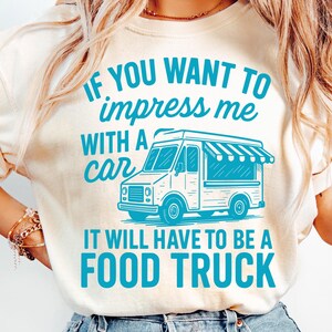 May include: Cream-colored t-shirt with the text "IF YOU WANT TO impress me WITH A car IT WILL HAVE TO BE A FOOD TRUCK" in turquoise. The graphic includes a food truck illustration.
