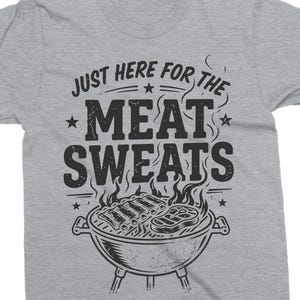 May include: A gray t-shirt with the phrase "JUST HERE FOR THE MEAT SWEATS" in black, above a graphic of a grill with ribs and steak. The shirt is a casual wear item.