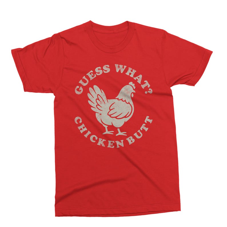 May include: Red t-shirt with a distressed graphic of a chicken and the text "GUESS WHAT? CHICKEN BUTT" in a circular design. The graphic is in a light, off-white color, contrasting with the solid red background of the shirt.