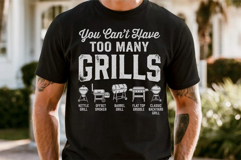 May include: Black t-shirt with the text "You Can't Have TOO MANY GRILLS" in white. Below the text are illustrations of different grill types: kettle, offset smoker, barrel, flat top griddle, and classic backyard grill.