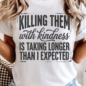 K&ouml;nnte beinhalten: Wei&szlig;es T-Shirt mit dem schwarzen Aufdruck "Killing them with kindness is taking longer than I expected". Der Text ist in einer Used-Schriftart gehalten. Das T-Shirt hat einen Rundhalsausschnitt und kurze &Auml;rmel.