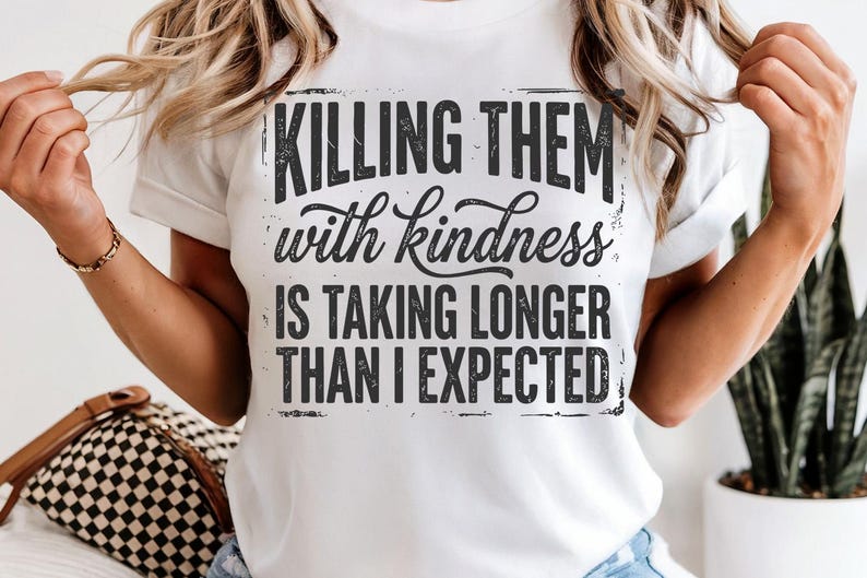 K&ouml;nnte beinhalten: Wei&szlig;es T-Shirt mit dem schwarzen Aufdruck "Killing them with kindness is taking longer than I expected". Der Text ist in einer Used-Schriftart gehalten. Das T-Shirt hat einen Rundhalsausschnitt und kurze &Auml;rmel.
