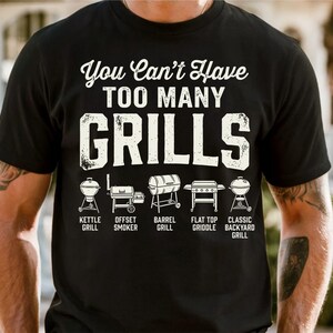 May include: Black t-shirt with the text "You Can't Have TOO MANY GRILLS" in white, above illustrations of different grill types: kettle, offset smoker, barrel, flat top griddle, and classic backyard grill.