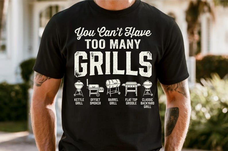 May include: Black t-shirt with the text "You Can't Have TOO MANY GRILLS" in white, above illustrations of different grill types: kettle, offset smoker, barrel, flat top griddle, and classic backyard grill.
