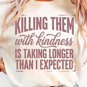 K&ouml;nnte beinhalten: Cremefarbenes T-Shirt mit dem Spruch "KILLING THEM with kindness IS TAKING LONGER THAN I EXPECTED" in einer verblassten, kastanienbraunen Schrift. Das Shirt hat einen Rundhalsausschnitt und kurze &Auml;rmel.