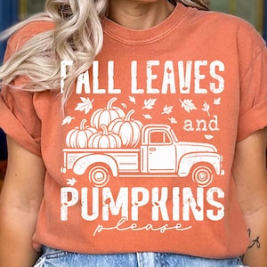 Könnte beinhalten: Ein orangefarbenes T-Shirt mit dem weißen Text "Fall Leaves and Pumpkins Please". Die Grafik zeigt einen weißen LKW mit Kürbissen und Herbstblättern. Das T-Shirt hat hochgekrempelte Ärmel.