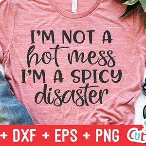 Może przedstawiać: R&oacute;żowa koszulka z nadrukiem "I'M NOT A hot mess I'M A SPICY disaster" w kolorze czarnym. Koszulka leży na białym tle z okularami przeciwsłonecznymi i kawałkiem dżinsu.