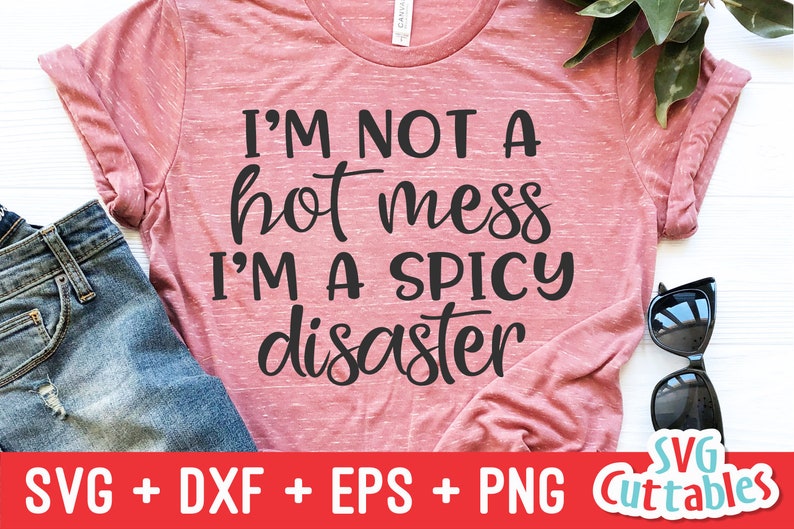 Może przedstawiać: R&oacute;żowa koszulka z nadrukiem "I'M NOT A hot mess I'M A SPICY disaster" w kolorze czarnym. Koszulka leży na białym tle z okularami przeciwsłonecznymi i kawałkiem dżinsu.