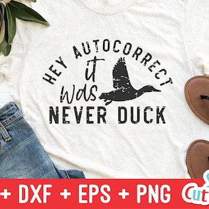 May include: A white t-shirt with the text "Hey it was never duck" in black lettering. The text is in a distressed font and includes a black silhouette of a duck.