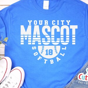 以下が含まれることがあります： 「YOUR CITY MASCOT SOFTBALL」と白で書かれたグラフィックデザインが施された青いTシャツ。中央には野球ボールと数字の18が描かれている。