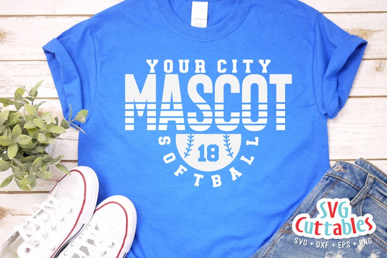 以下が含まれることがあります： 「YOUR CITY MASCOT SOFTBALL」と白で書かれたグラフィックデザインが施された青いTシャツ。中央には野球ボールと数字の18が描かれている。