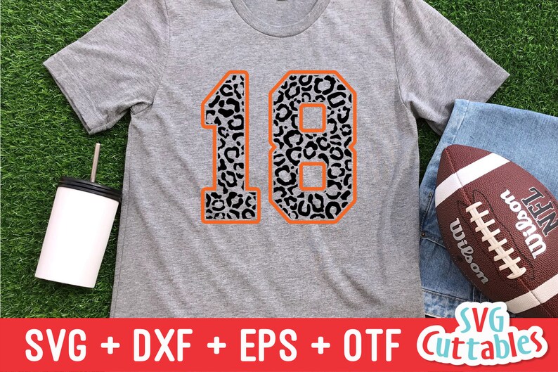 Puede incluir: Una camiseta gris con un gran n&uacute;mero 18 de contorno naranja. Los n&uacute;meros est&aacute;n rellenos con un patr&oacute;n de estampado de leopardo blanco y negro.