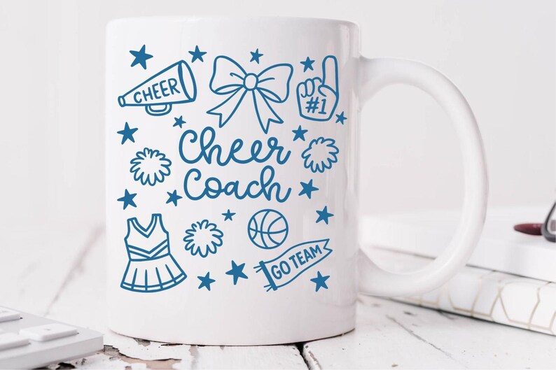May include: White ceramic mug with a blue design featuring cheerleading-related graphics and text. The design includes a megaphone, bow, pom-poms, a jersey, a basketball, stars, and the words "Cheer Coach" and "Go Team".