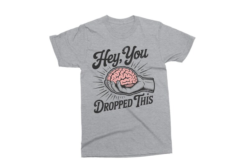 May include: A light gray t-shirt with the text "Hey, You Dropped This." The graphic features a pink brain held in a hand, with radiating lines. The design is in black and white.