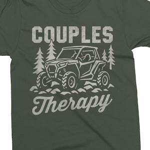 May include: Dark green t-shirt with a white graphic. The graphic features the words "COUPLES Therapy" above and below a line drawing of an off-road vehicle and two pine trees. The shirt is made of a soft material.
