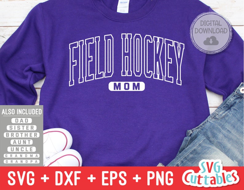 May include: Purple sweatshirt with the text "FIELD HOCKEY MOM" in white outlined letters. The sweatshirt is on a wooden surface with a pair of white sneakers and blue jeans.