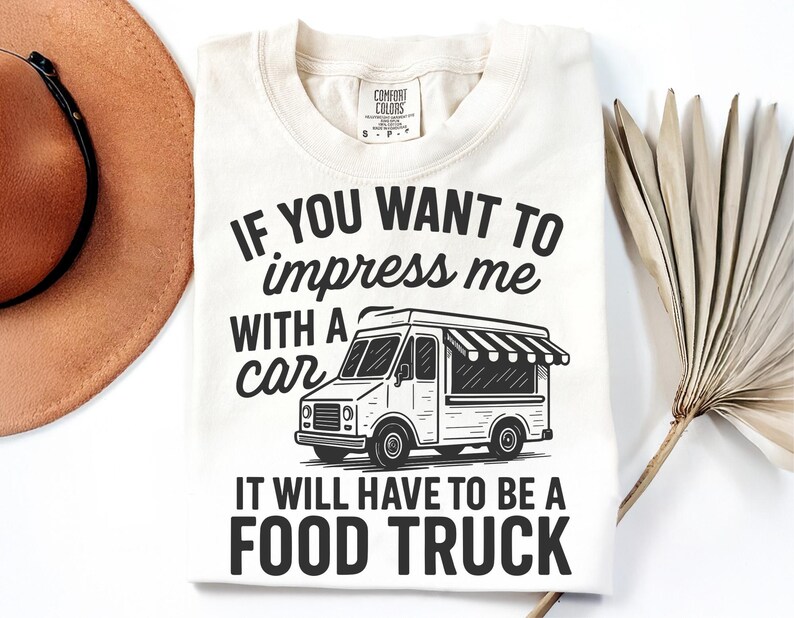 May include: Cream-colored t-shirt with the text "IF YOU WANT TO impress me WITH A car IT WILL HAVE TO BE A FOOD TRUCK" in black. The graphic includes a food truck illustration.