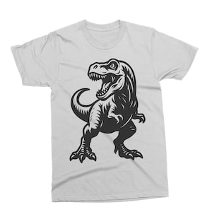 May include: White t-shirt featuring a black graphic of a Tyrannosaurus Rex. The dinosaur is depicted with an open mouth, showing teeth, and is in a standing pose. The shirt is made of a soft material.
