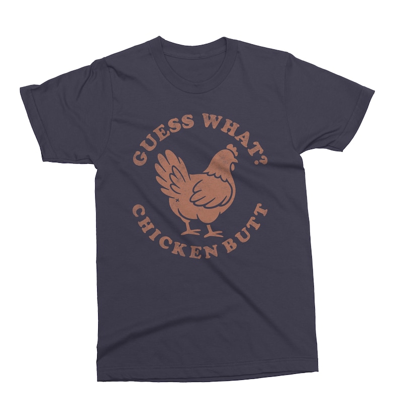 May include: Navy blue t-shirt with a brown graphic of a chicken and the text "GUESS WHAT? CHICKEN BUTT" in a circular design. The shirt is a crew neck style.