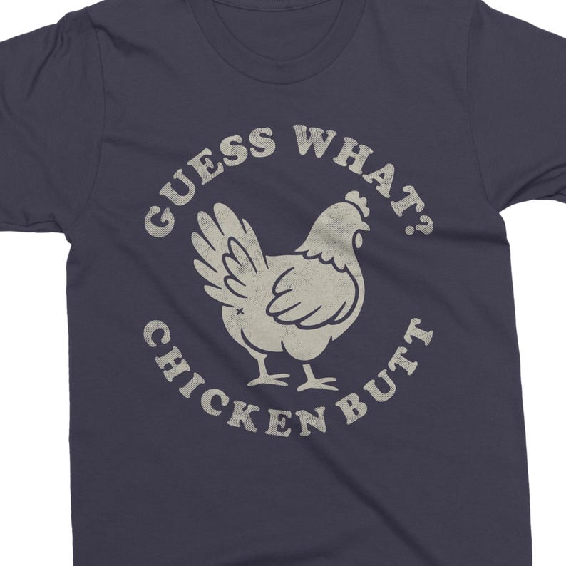 May include: Navy blue t-shirt with a distressed graphic of a chicken and the text "GUESS WHAT? CHICKEN BUTT" in a circular design. The chicken is light beige, and the text is in a vintage style.