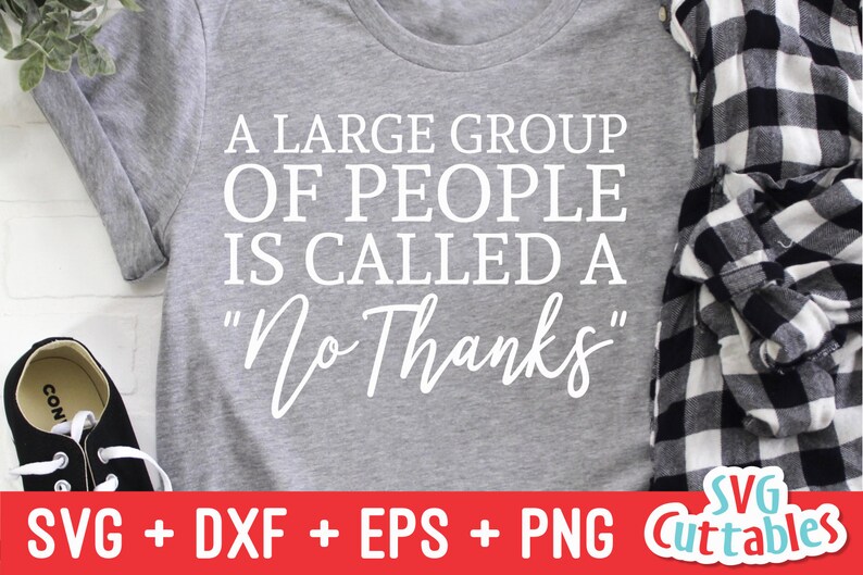 Może przedstawiać: Szary T-shirt z nadrukiem "A large group of people is called a "No Thanks"" w kolorze białym. T-shirt leży na białej powierzchni z cegły, obok znajduje się koszula w kratę i czarno-białe buty.