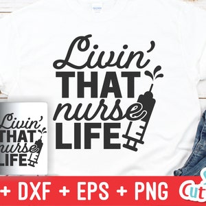 Pu&ograve; includere: Una maglietta bianca con testo nero che recita "Livin' THAT nurse LIFE" con un'immagine di una siringa. La maglietta &egrave; esposta su una superficie di legno con una tazza bianca e jeans blu.