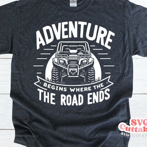 May include: A dark gray t-shirt with a white graphic design of an ATV and the text "Adventure Begins Where The Road Ends".