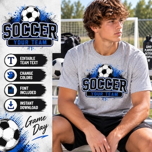 May include: A heather gray t-shirt featuring a graphic of a black and white soccer ball above the text SOCCER YOUR TEAM in bold blue and black lettering. The design includes blue paint splatter accents and a clean, modern aesthetic.