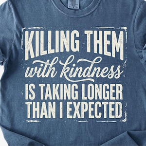 K&ouml;nnte beinhalten: Ein marineblaues T-Shirt mit dem wei&szlig;en Aufdruck &bdquo;KILLING THEM with kindness IS TAKING LONGER THAN I EXPECTED&ldquo; im Used-Look. Das Shirt hat hochgekrempelte &Auml;rmel und einen Rundhalsausschnitt.